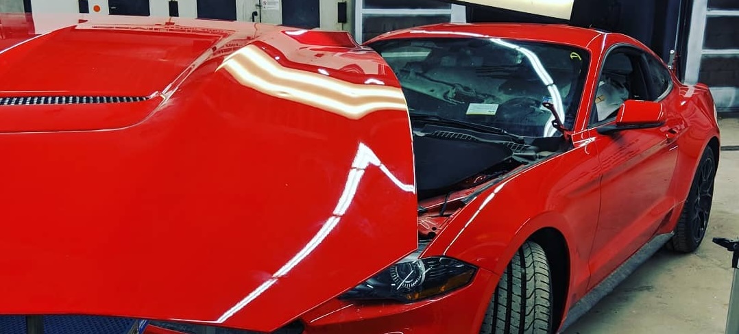 Red Ford Mustang with its hood raised beneath paintless dent repair inspection lights