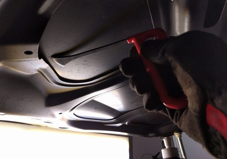 Specialized hand tool reaching behind a vehicle panel during dent repair